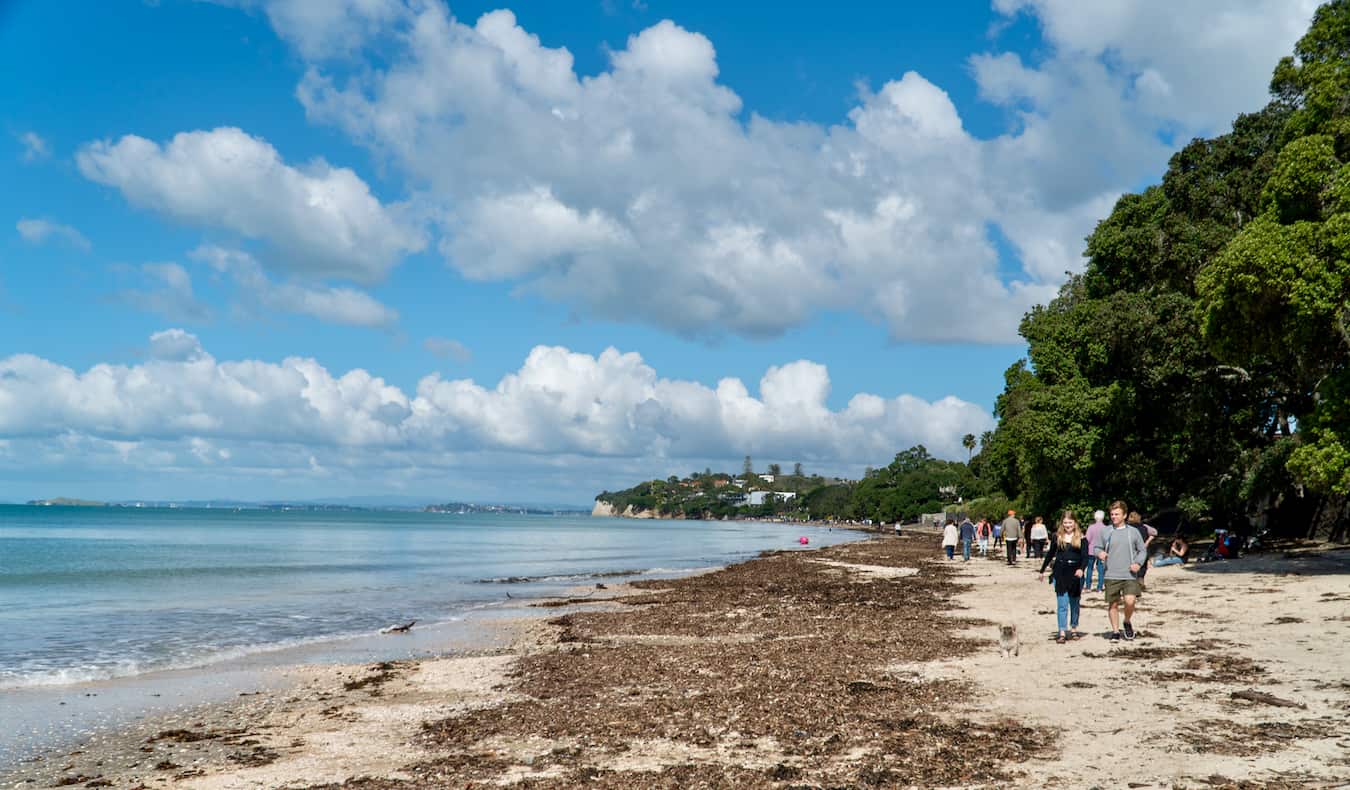 Gente caminando por la ancha playa cerca de Takapuna en Auckland, Nueva Zelanda