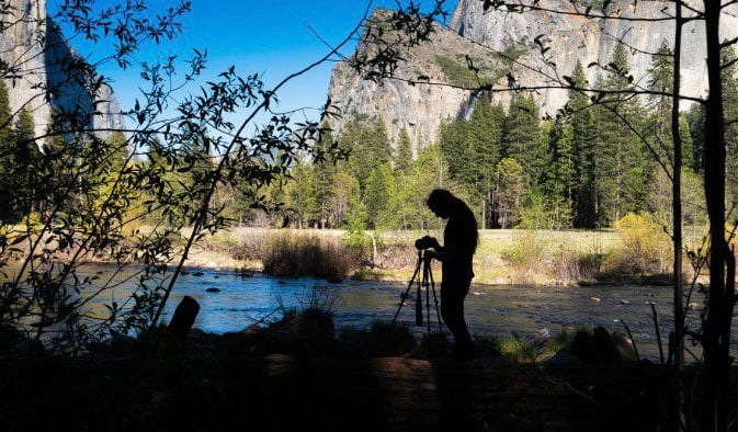 Fotógrafo profesional preparándose para tomar una foto de viaje a la naturaleza con un cielo azul