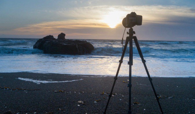 Trípode y cámara instalados en una playa natural en el extranjero durante una puesta de sol relajante