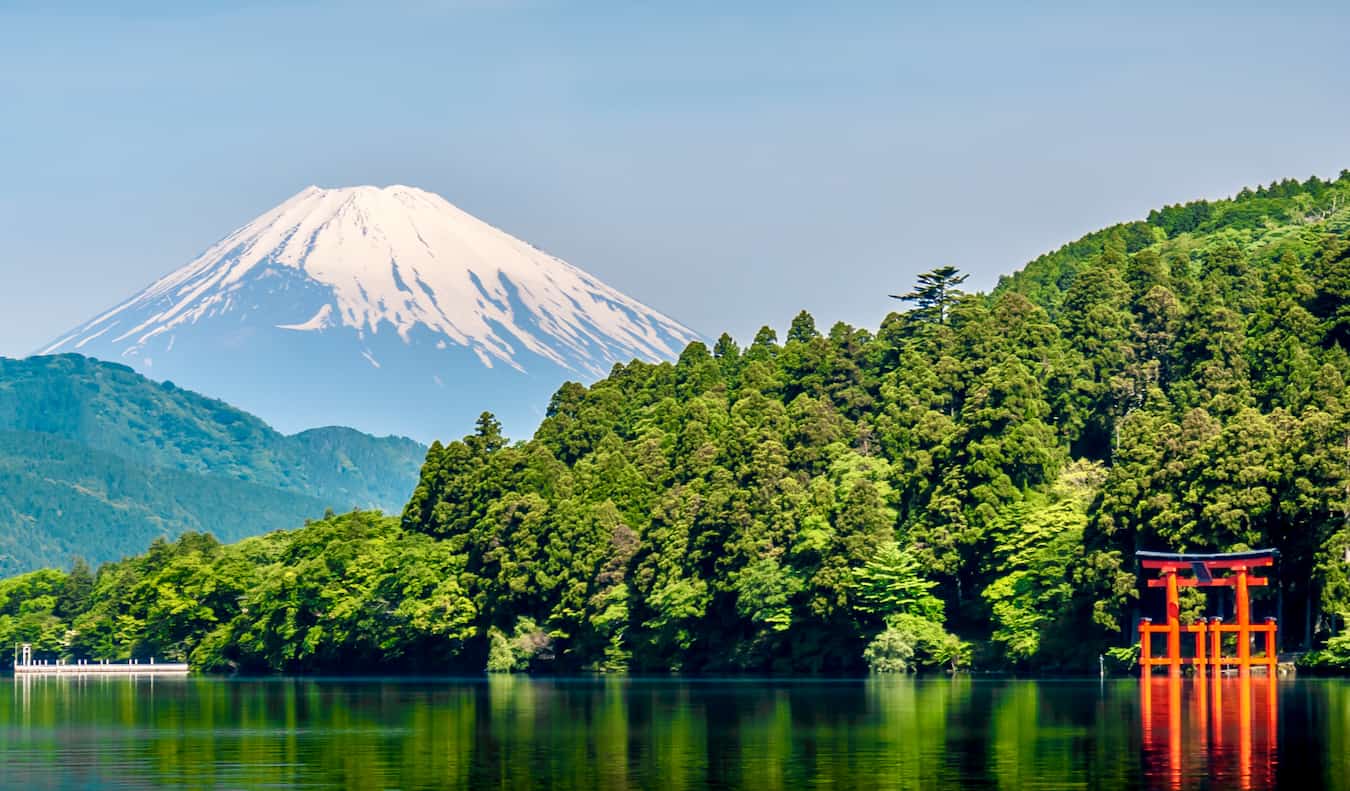 Una puerta torii roja en el agua con una vegetación exuberante y el monte Fuji en el fondo Japón