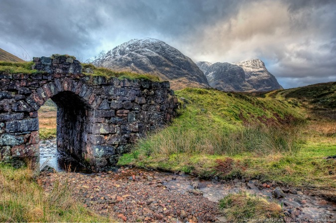 Fotografía cautivadora de una puerta de pared de piedra y cordillera en la Europa lluviosa