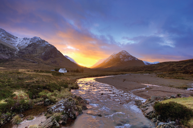 Foto de la puesta de sol detrás de las montañas en Glencoe, Escocia, con una casa en medio del terreno