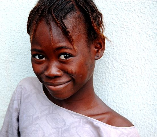 Una chica negra joven de pie cerca de una pared blanca posando