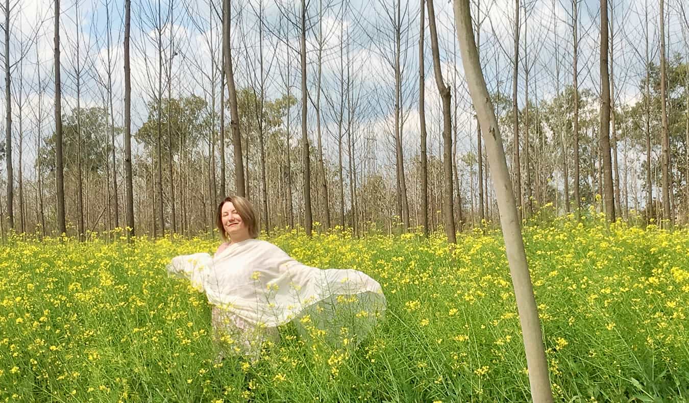 Una mujer sola en la India poniendo en un campo verde rodeado de hierba y árboles