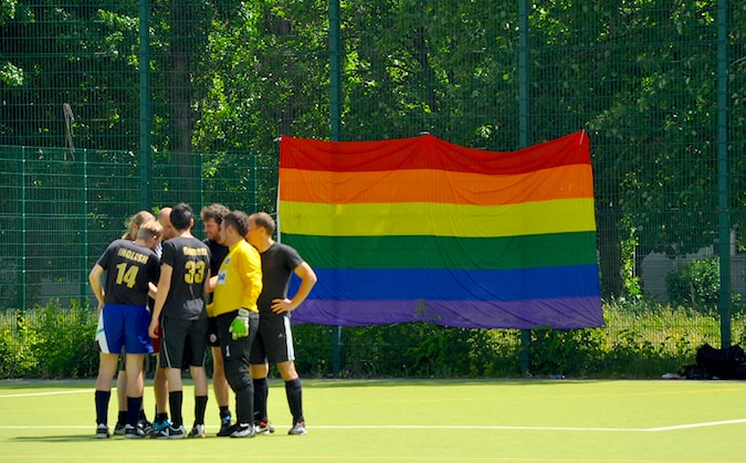 Un equipo de fútbol de pie en un campo con una bandera del orgullo enorme al fondo