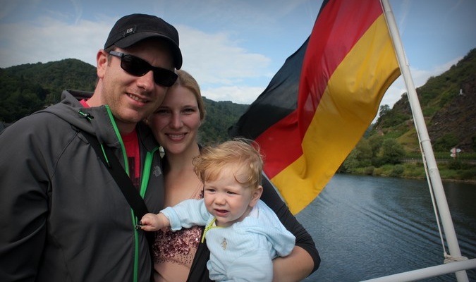 Familia de tres personas que viajan poniendo con una bandera alemana