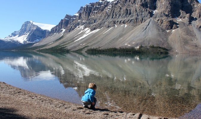 El niño pequeño se inclina por tocar el hermoso lago en el extranjero