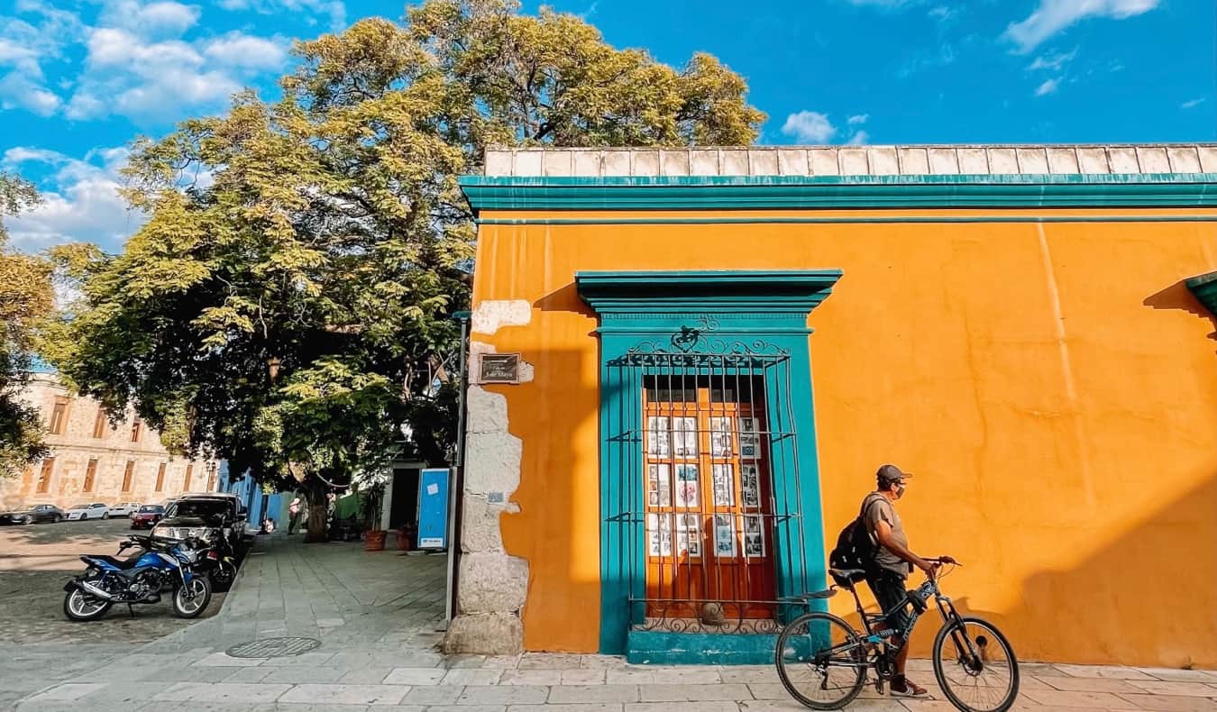 Un hombre local en Oaxaca, México, con una bicicleta cerca de un edificio coloreado