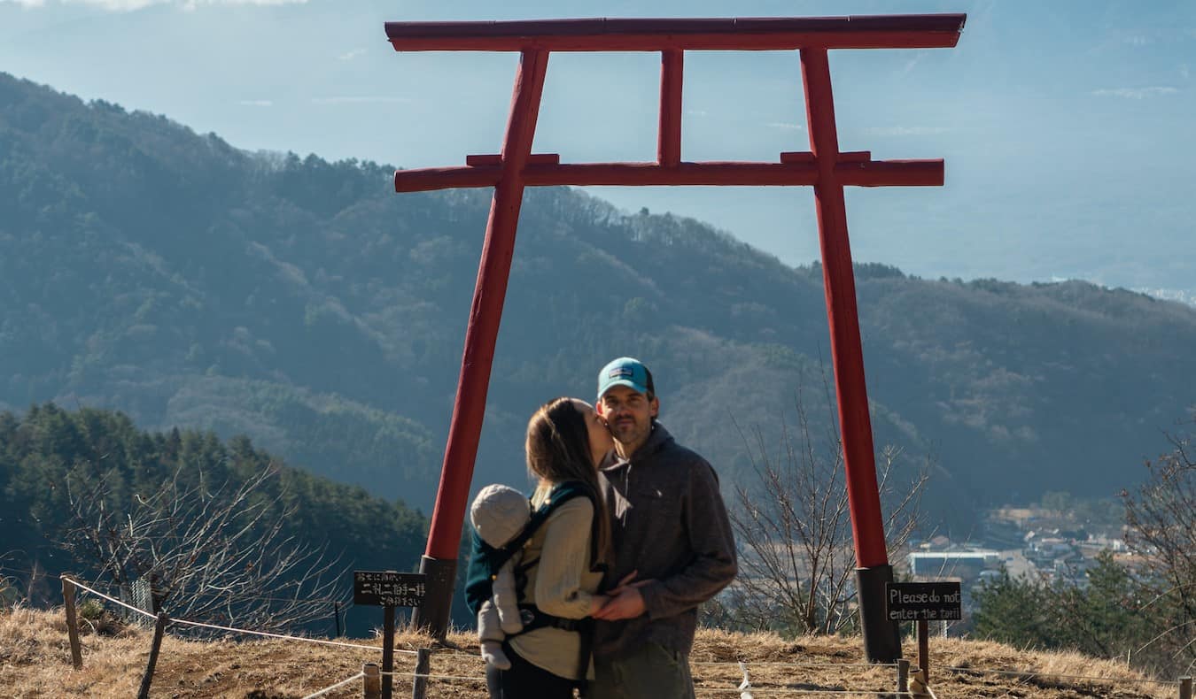 La blogger Kristin Addis de Be My Travel Muse con su pareja y su bebé bajo un arco torii en Japón