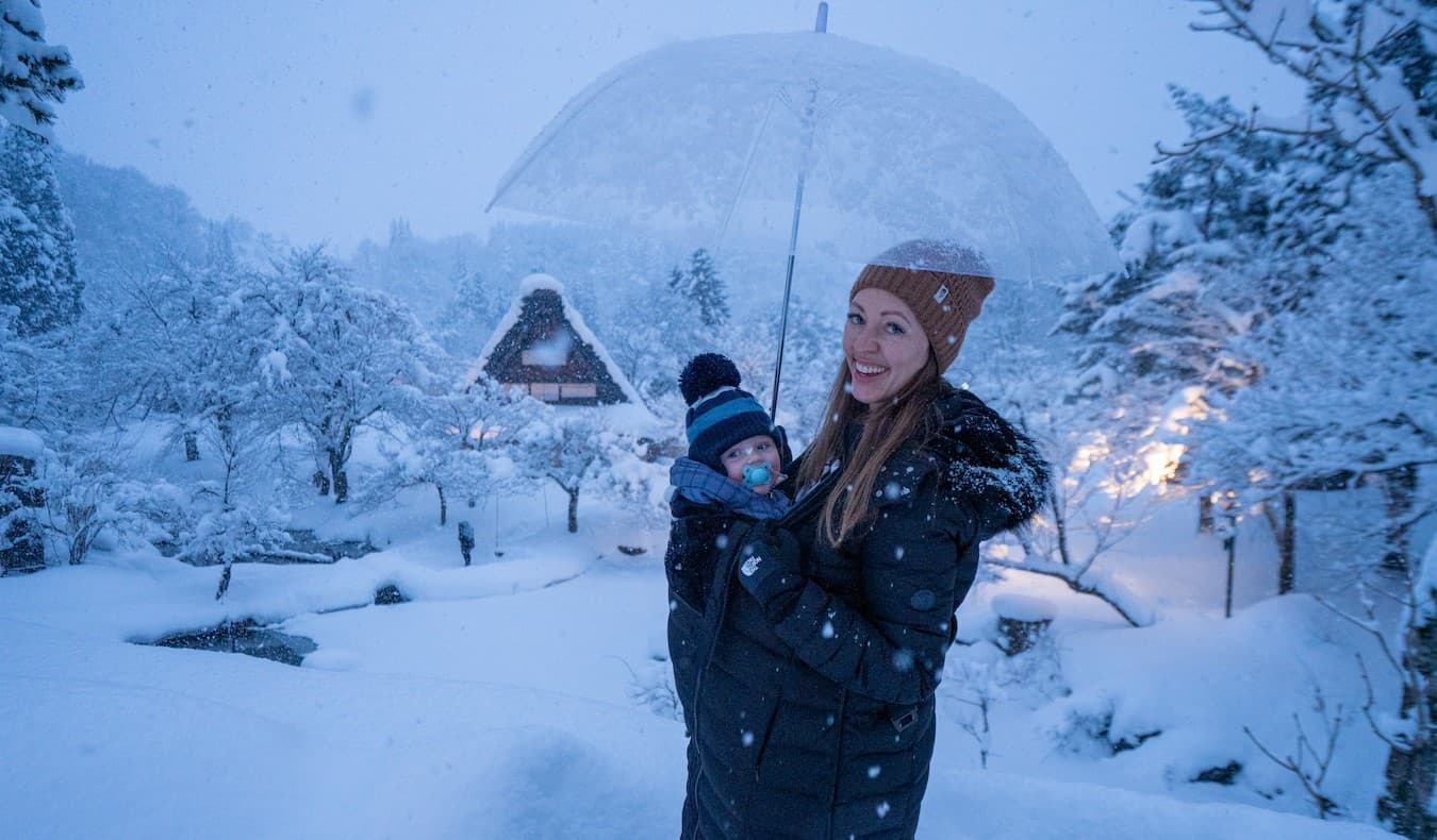 La bloguera Kristin Addis de Be My Travel Muse con su hijo pequeño en un portabebé mientras se encuentran en un paisaje nevado en Japón