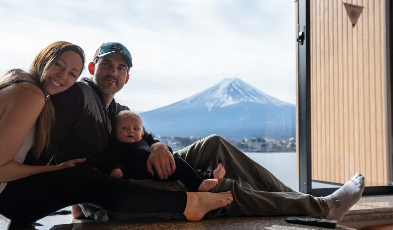 La blogger Kristin Addis de Be My Travel Muse junto a su pareja y su bebé sentado junto a una ventana en Japón con una montaña nevada al fondo