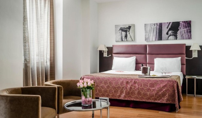 Una habitación con acentos rosados ​​en todas partes, incluidas rosas en un jarrón sobre una mesa baja en el hotel Eurostars Roma Aeterna de Roma, Italia