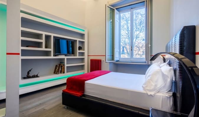 Una habitación sencilla con una cama frente a un centro de entretenimiento que incluye estanterías y un televisor en el hotel Luxury on the River de Roma, Italia