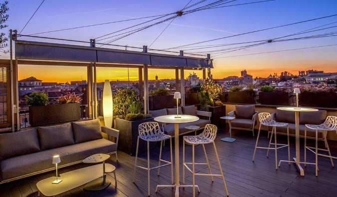 Bar y salón en la azotea con el paisaje urbano al fondo justo después de la puesta de sol en el Monti Palace Hotel de Roma, Italia