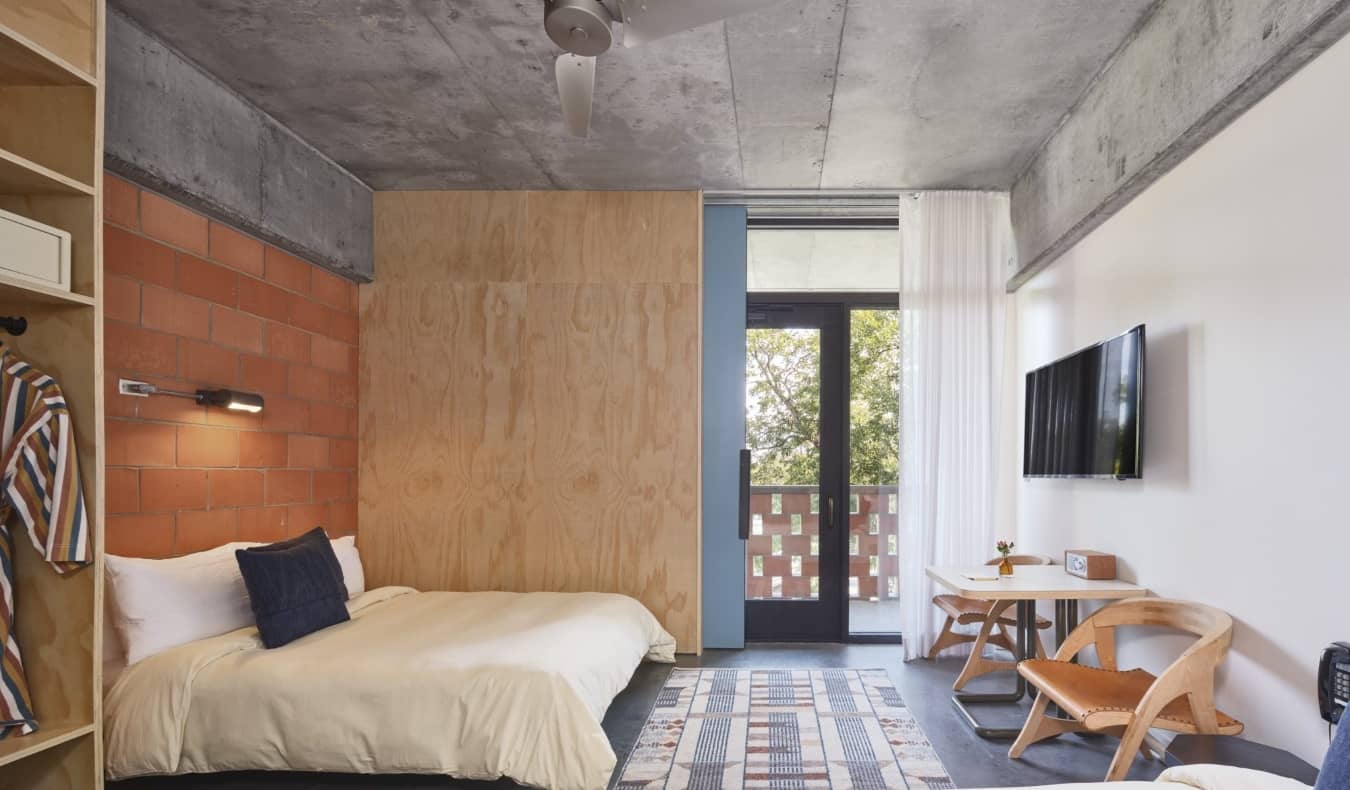 Habitación con pared de ladrillo visto, terraza y escritorio de madera en el The Carpenter Hotel de Austin, Texas