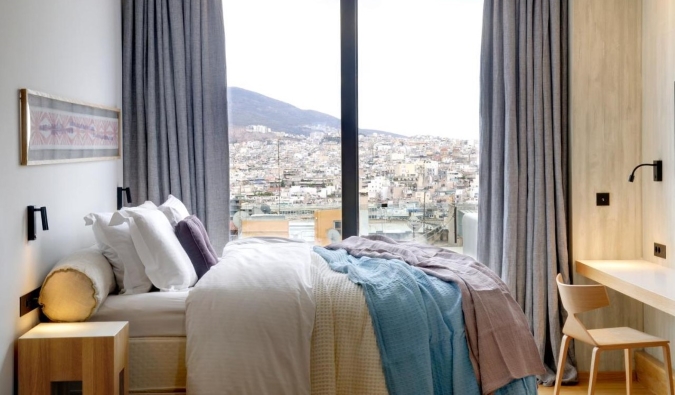 Habitación sencilla pero acogedora en el hotel Coco-Mat con ventanas de suelo a techo con vistas a la ciudad de Atenas, Grecia