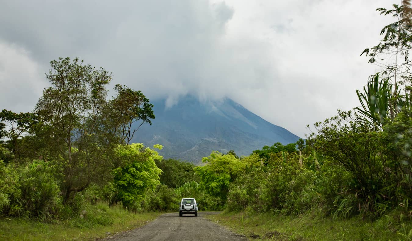 Un coche circulando por un camino de tierra a la sombra del volcán Arenal en Costa Rica