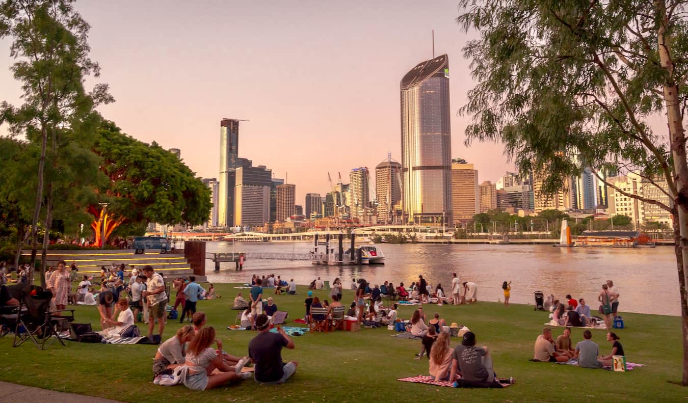 Gente relajándose a orillas del South Bank cerca del agua mirando hacia el CBD de Brisbane, Australia