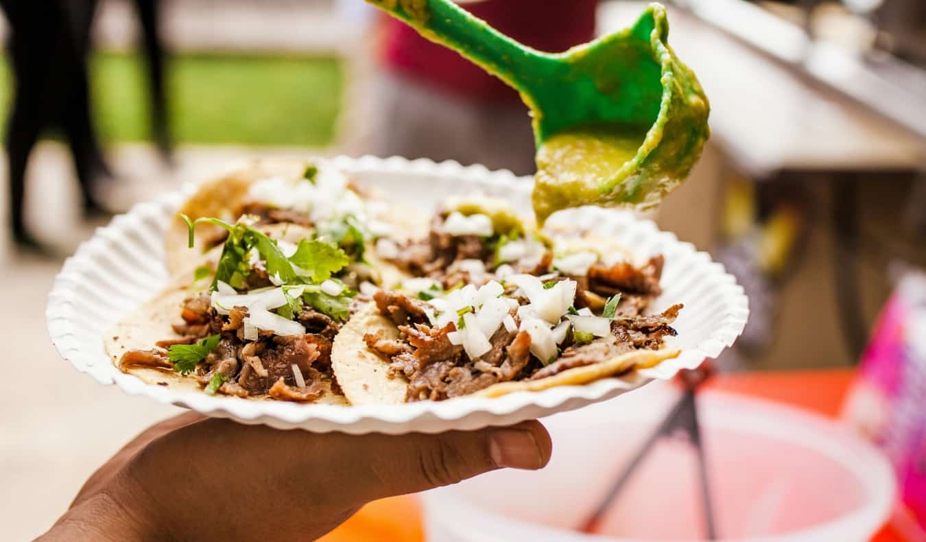 Una mano sosteniendo un plato de papel lleno de tacos frescos en Ciudad de México, México