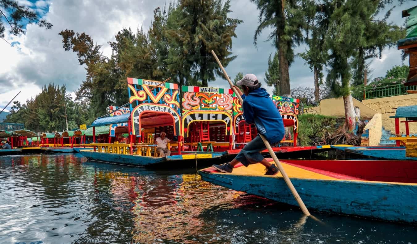 Un niño empuja un barco de colores por un río con un palo largo en los canales de Xochimilco en Ciudad de México, México