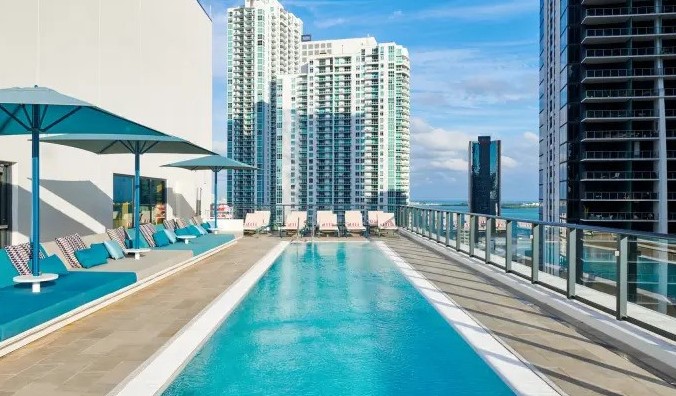 Piscina rectangular larga en la azotea con hamacas junto a la piscina, rodeada por los rascacielos de Miami, Florida, en el hotel citizenM Miami Brickell