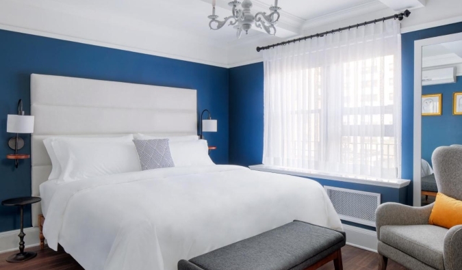 Habitación de hotel sencilla con paredes azules profundas, una araña y una silla junto a una cama grande en el hotel voco The Franklin de Nueva York