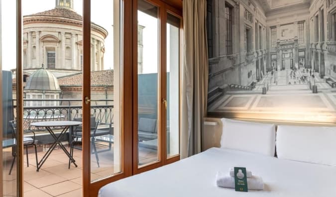 Una cama doble en una habitación de hotel con una puerta abierta que da a una terraza con vistas a una B&B Hotel Milano Sant'Ambrogio, un hotel de Milán, Italia