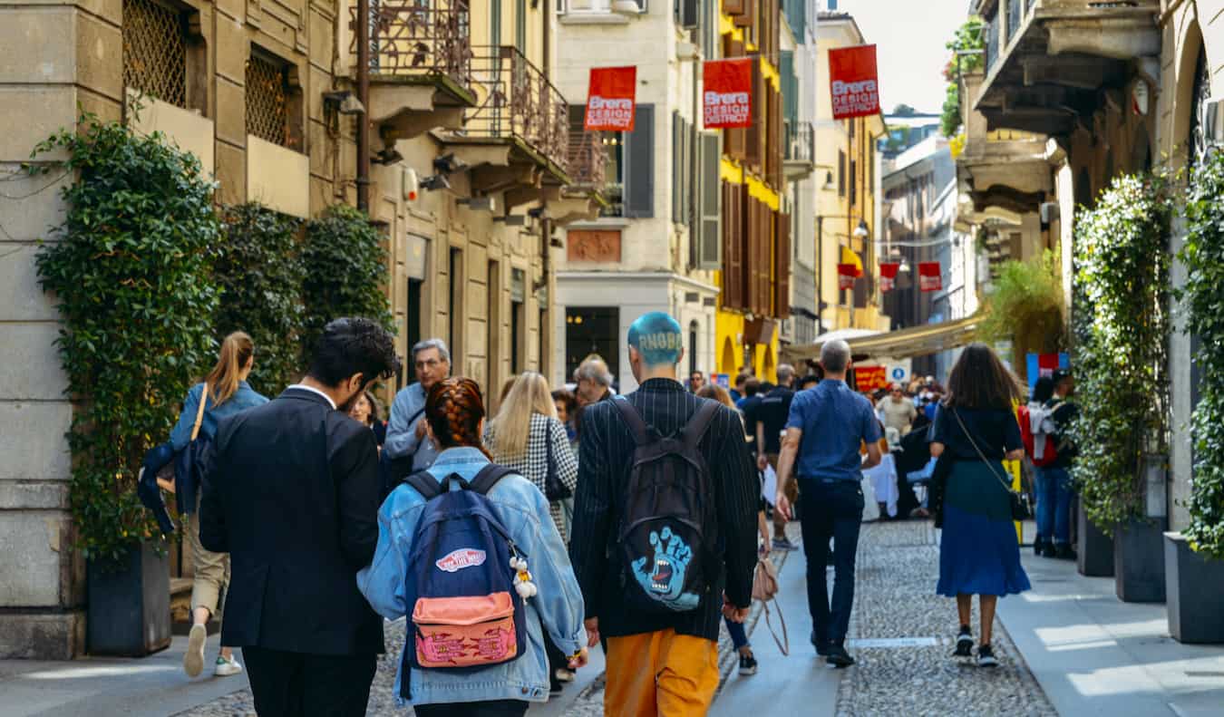 Gente caminando por una calle estrecha rodeada de tiendas y cafeterías en la bulliciosa Milán, Italia