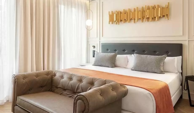 Una prenda de decoración dorada cuelga sobre una cama doble con un asiento de amor a los pies de la cama del Hotel Catalonia Goya en Madrid, España