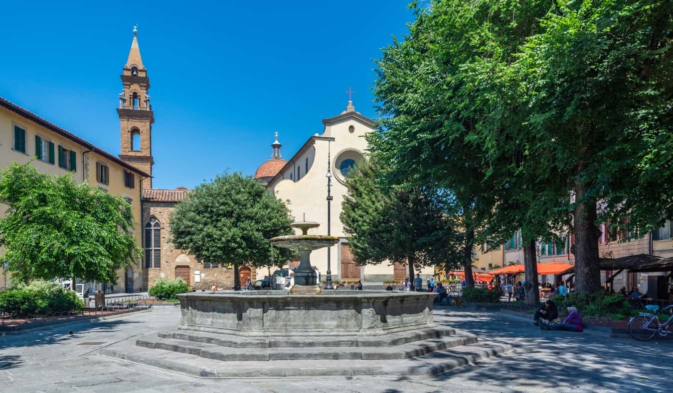 Gente sentada en torno a una fuente en la frondosa plaza de Santo Spirito en la zona del Oltrarno de Florencia, Italia