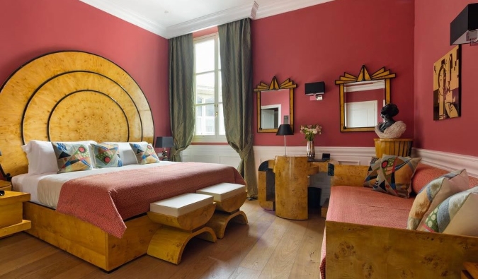 Una habitación de hotel con paredes de color salmón vibrante y una cama, escritorio y espejos, todo con un estilo art déco de madera original en La Maison du Sage, un hotel de Florencia, Italia.