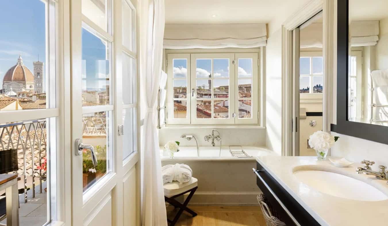 Un baño de lujo lleno de una gran bañera, suelos de madera y ventanas con vistas al Duomo desde uno de ellos en The Place, un hotel de cinco estrellas en Florencia, Italia.