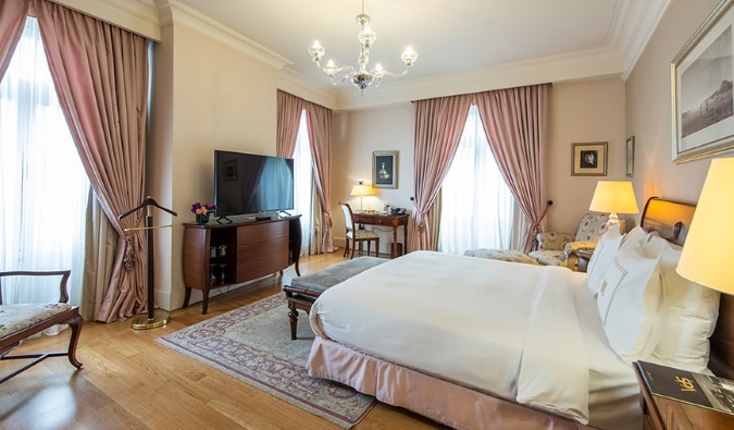 Una gran habitación con ventanas adornadas con cortinas de color rosa, suelos de madera dura y otros elementos históricos en el Pera Palace Hotel de Estambul, Turquía