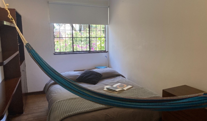 Habitación sencilla en Magdalena Guest House en Bogotá, Colombia, con cama doble, armario de madera, ventana y hamaca en la otra habitación.