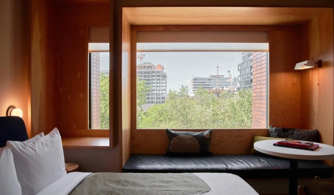 Una cama frente a un ventanal en una pared con paneles de madera, con un banco de ventana frente al Ace Hotel de Toronto, Canadá