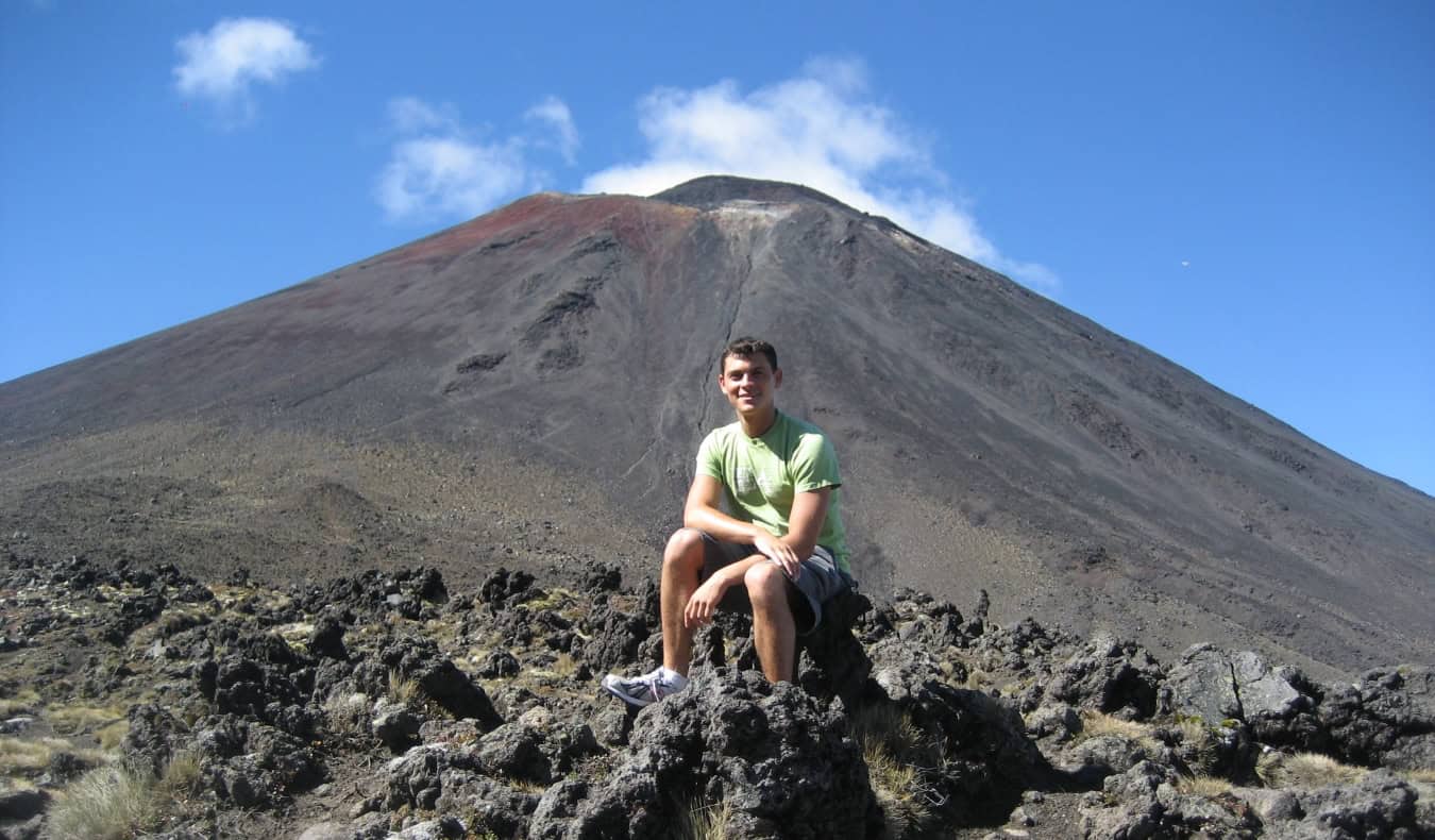 El blogger Nomadic Matt sentado frente al monte Ngauruhoe, un cono volcánico en el parque nacional de Tongariro, Nueva Zelanda