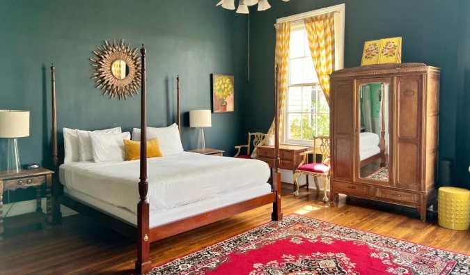 Una habitación con paredes de color verde intenso, suelos de madera, una cama con dosel, armario de madera y grandes ventanales en el Creole Gardens Inn, un hotel de Nueva Orleans, Luisiana