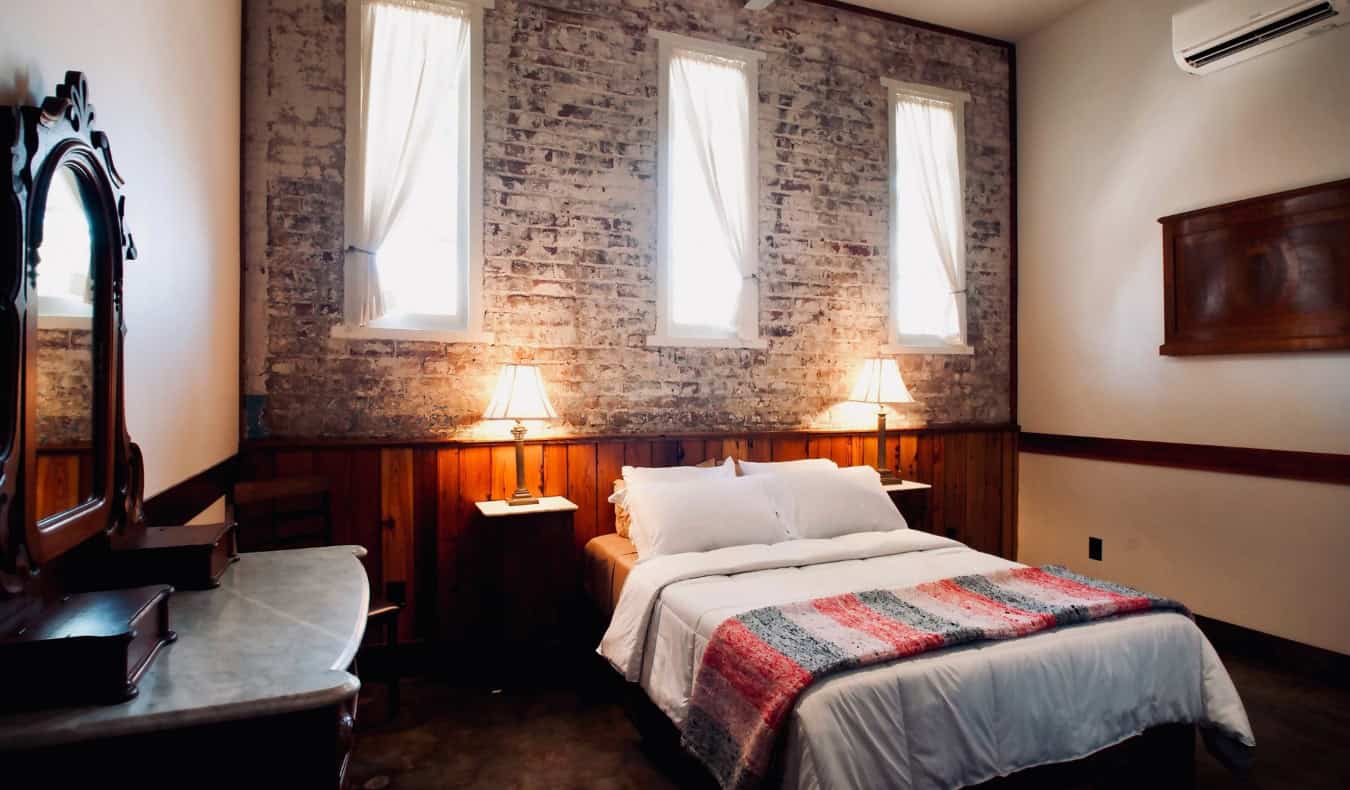 Una cama grande en una habitación con paredes de ladrillo visto y muebles antiguos en The Inn at the Old Jail, un hotel de Nueva Orleans, Luisiana